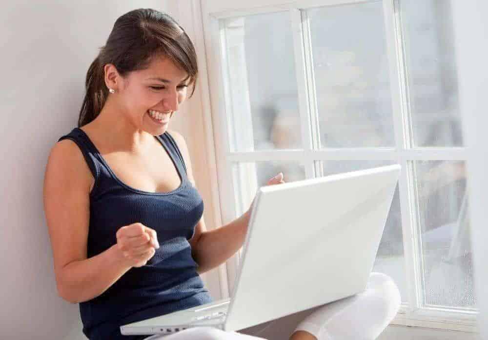 Woman sitting by a window with a laptop enjoying her online success